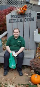 A young, smiling man sits in a large Adirondack chair wearing an OhioHealth polo shirt 